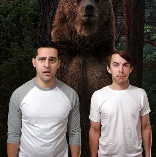 Two young men with confused expressions stand in front of a grizzly bear