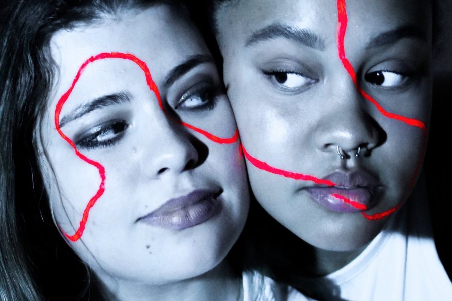 Two woman make eye contact. A winding red line is drawn across their faces.